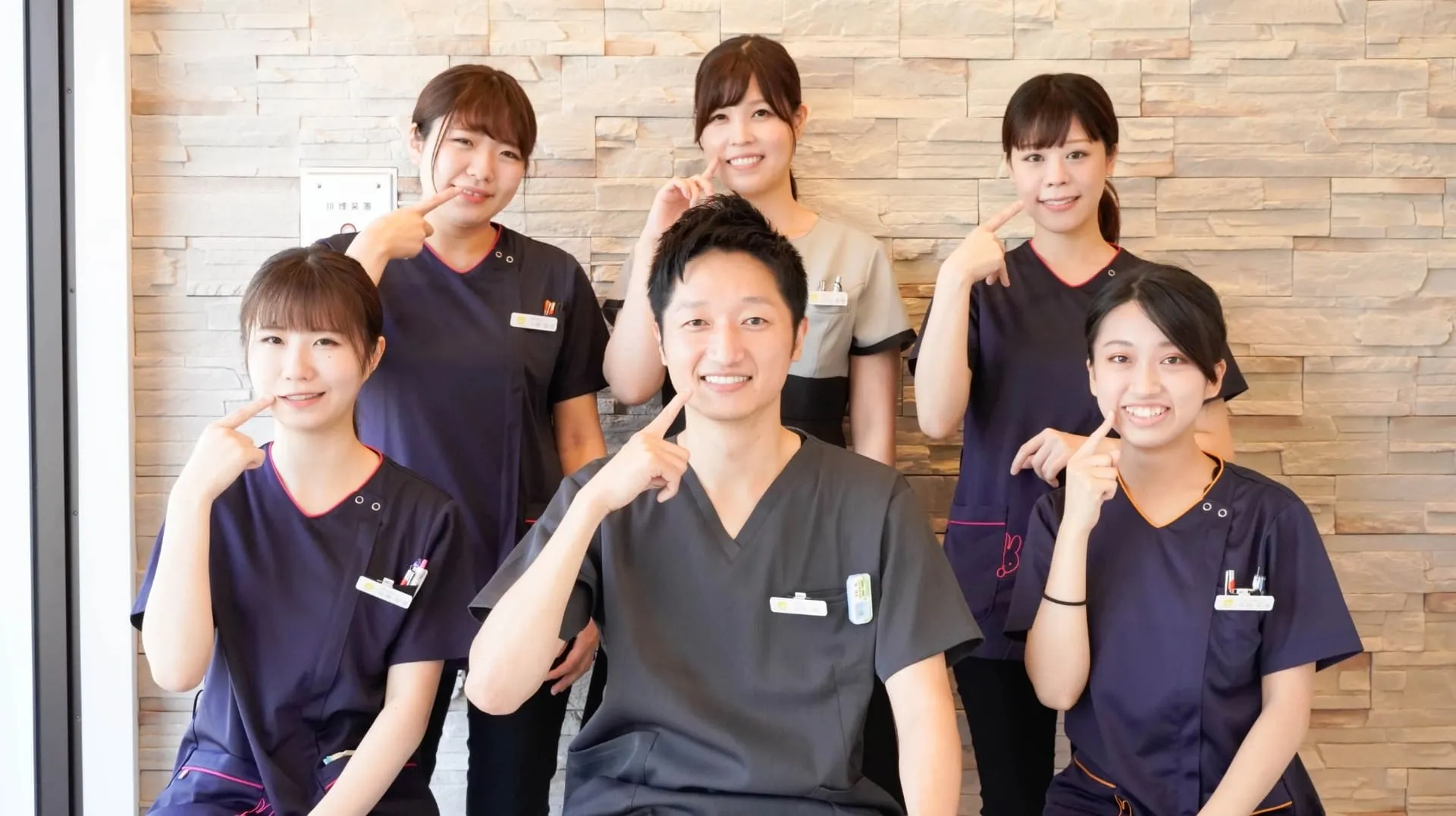 中央に男性歯科医師、取り囲むように歯科助手の女性が笑顔で座っている写真